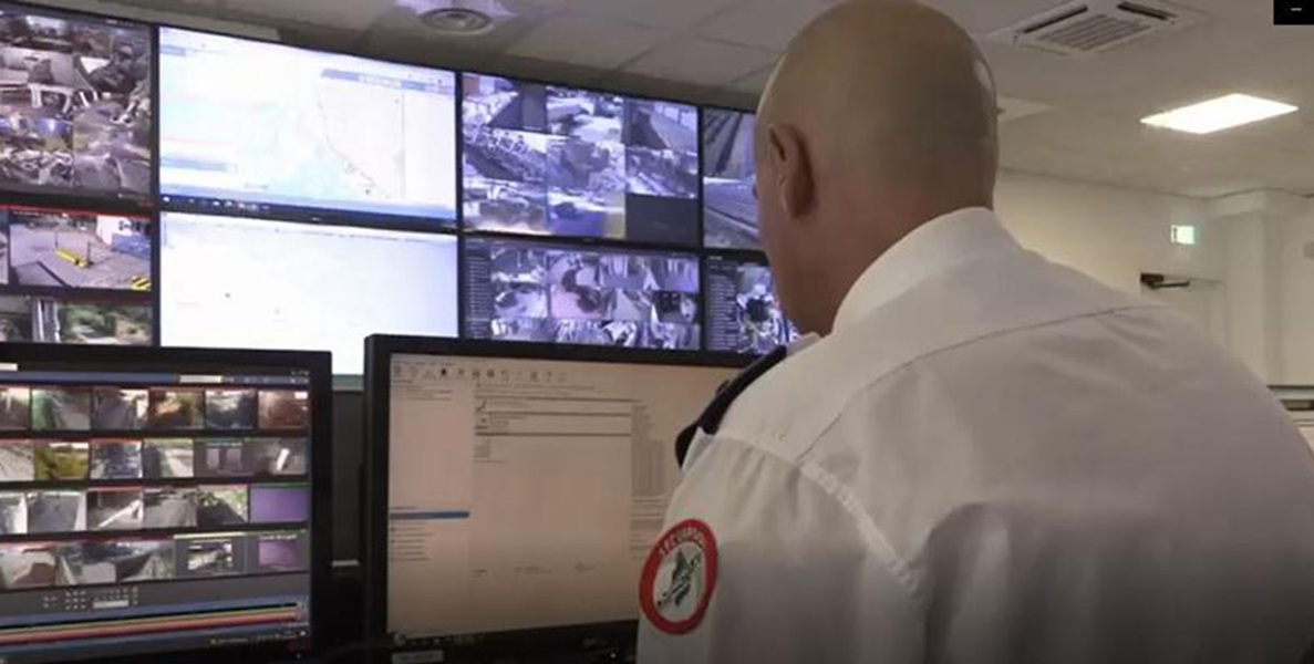 Operatore con stemma Securpool sulla camicia bianca osserva una parete di monitor con riprese di telecamere e una mappa